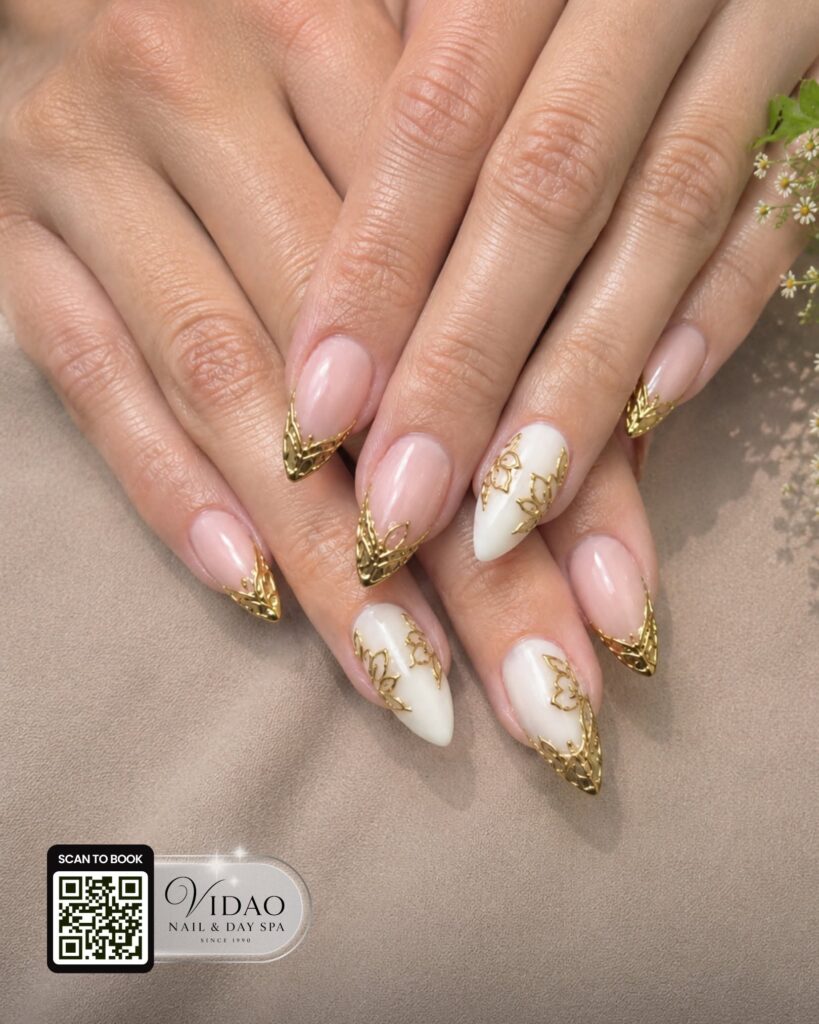 Nude and white almond nails with gold glitter tips and floral accents
